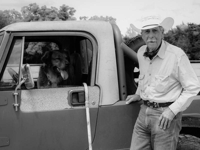 Sepia-toned portrait of a man in a cowboy hat leaning on a vintage truck — A Life Well Lived session by BK Bennett