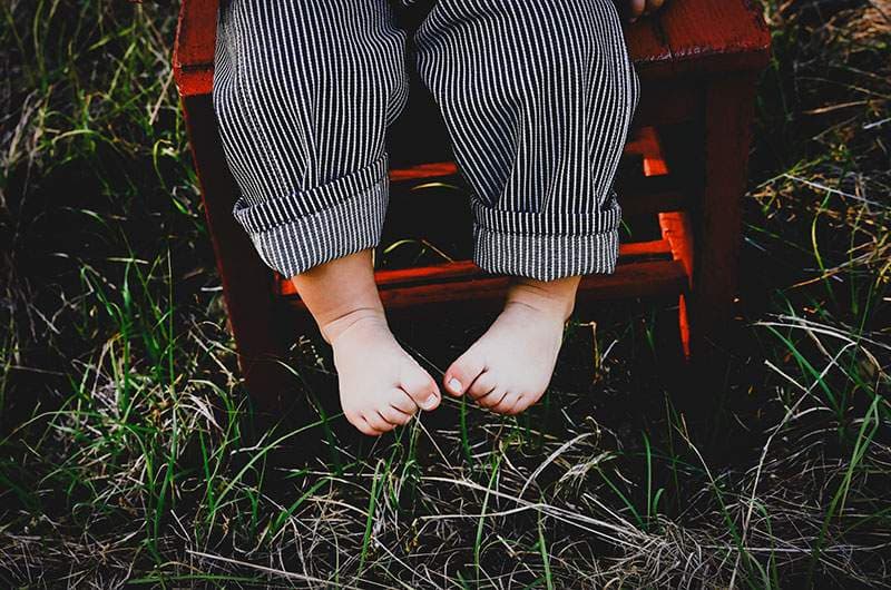 Baby's bare feet dangling from a red wagon in tall grass — Plano newborn photography by BK Bennett