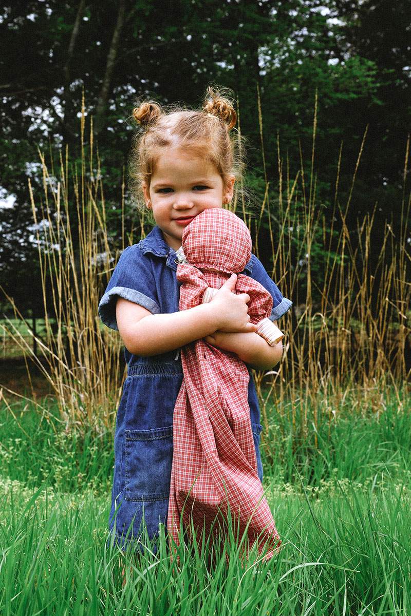 Little girl in a denim dress hugging a rag doll in tall grass — Frisco little-ones photography by BK Bennett
