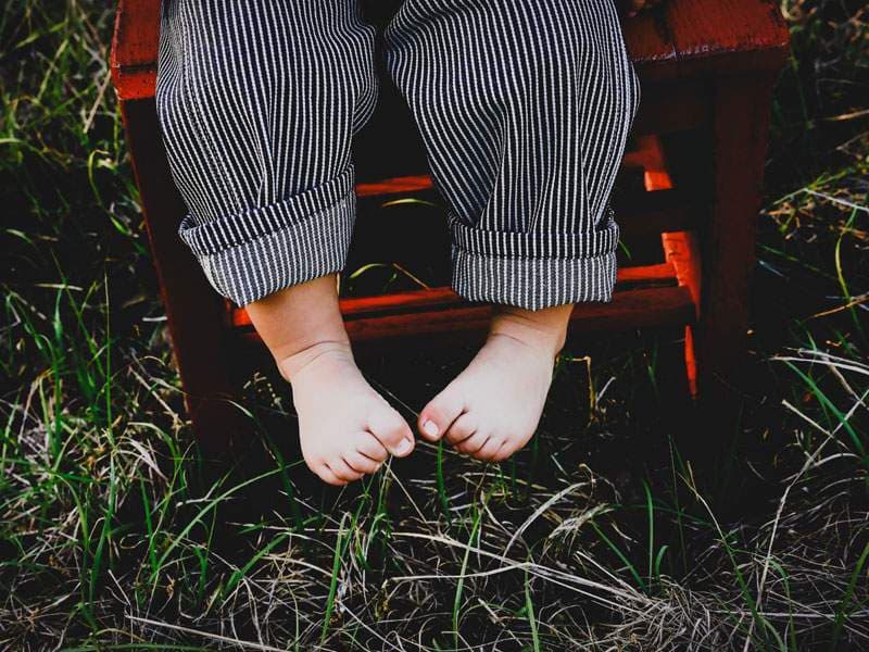 Bare toddler feet dangling from a red wooden stool in tall grass — newborn and little-ones portrait session by BK Bennett