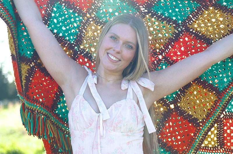 Smiling senior holding a colorful blanket outdoors — Frisco senior portraits by BK Bennett