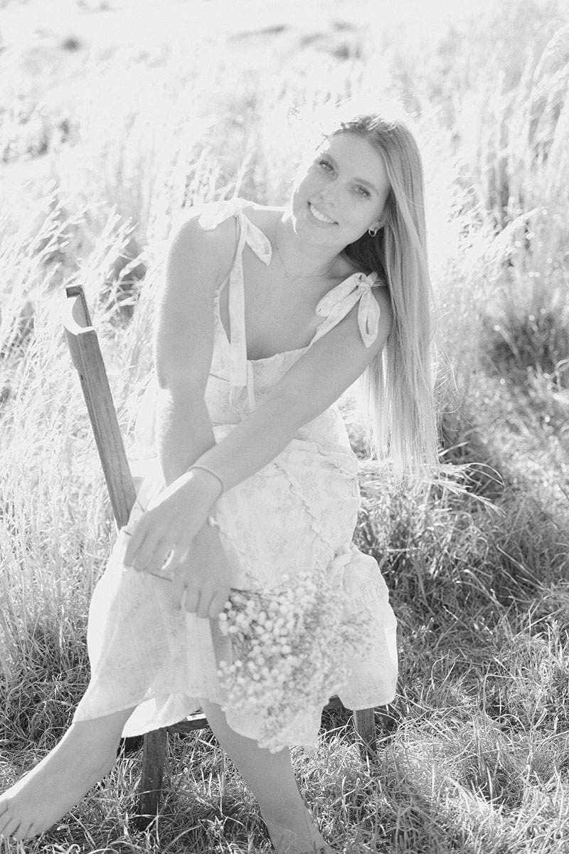 Black-and-white senior portrait holding baby's breath in tall grass — Arlington senior photographer BK Bennett