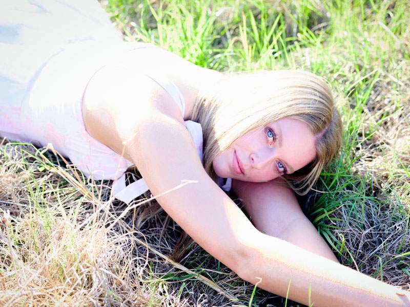 High school senior portrait of a young woman in a white dress lying in sunlit Texas grass — senior photography by BK Bennett
